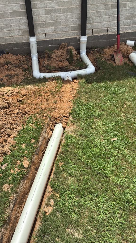 Buried downspout tie-ins connected to a solid PVC drain line along a brick home in Katy, TX